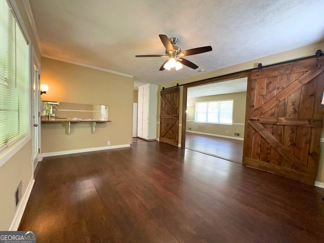 unfurnished living room with a barn door, dark wood finished floors, ceiling fan, and baseboards