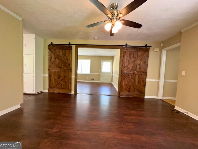 empty room with a barn door, baseboards, ceiling fan, wood finished floors, and a textured ceiling