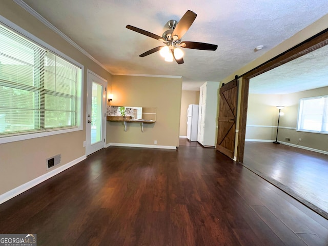 unfurnished living room with a barn door, dark wood-type flooring, a ceiling fan, baseboards, and crown molding