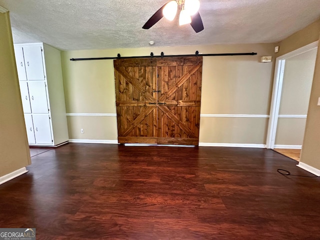 empty room with a ceiling fan, wood finished floors, a textured ceiling, baseboards, and a barn door