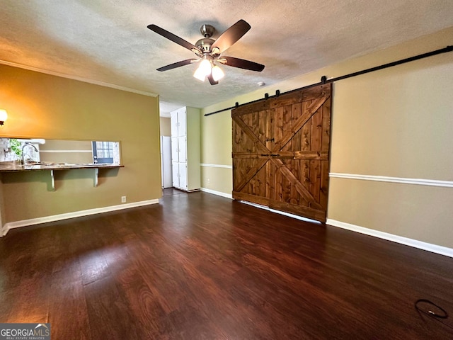 unfurnished living room featuring a barn door, a textured ceiling, ceiling fan, wood finished floors, and baseboards