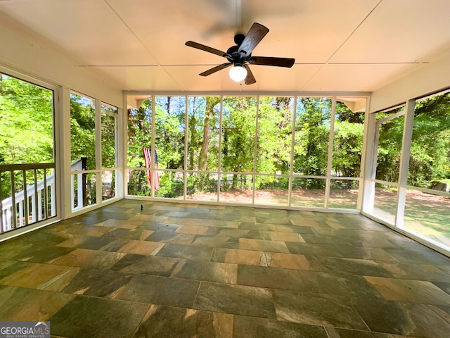 unfurnished sunroom featuring ceiling fan, stone tile floors, and view of wooded area