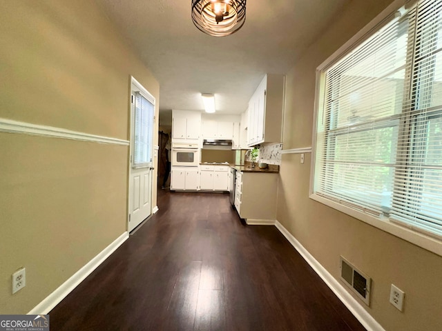 kitchen featuring oven, dark wood-type flooring, white cabinets, under cabinet range hood, and baseboards