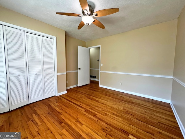 unfurnished bedroom featuring hardwood / wood-style floors, baseboards, a closet, a textured ceiling, and ceiling fan