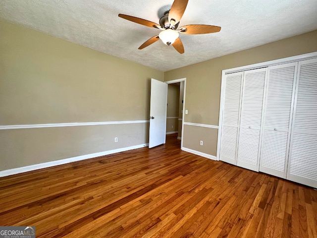 unfurnished bedroom featuring a textured ceiling, wood finished floors, baseboards, a closet, and ceiling fan
