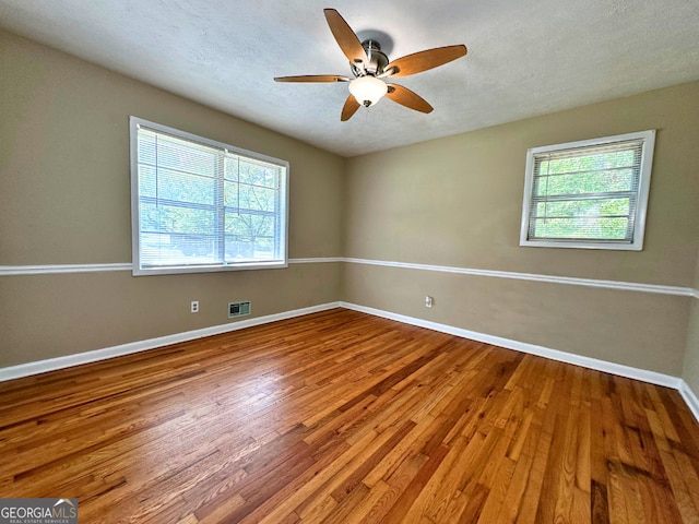 empty room featuring healthy amount of natural light, wood finished floors, baseboards, ceiling fan, and a textured ceiling