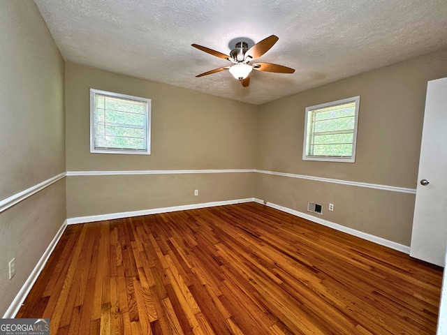 empty room with hardwood / wood-style flooring, healthy amount of natural light, a ceiling fan, a textured ceiling, and baseboards