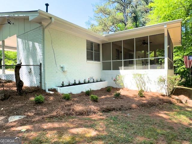 view of property exterior with brick siding, a sunroom, and a ceiling fan