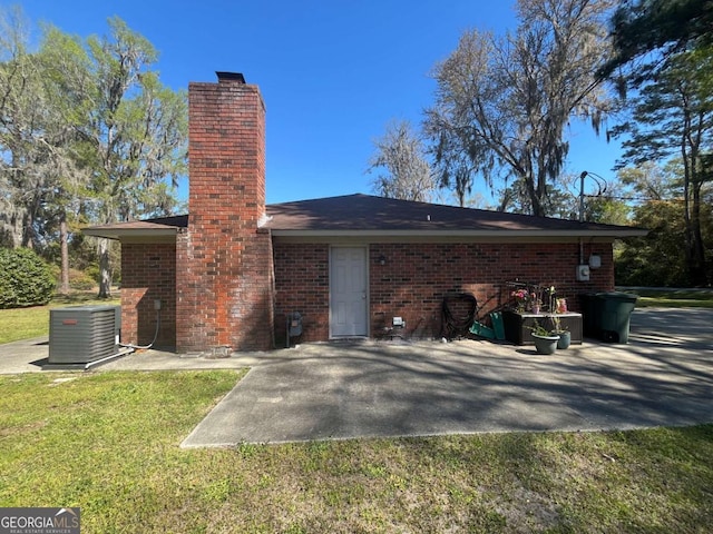 411 Woodland Dr, Hinesville, GA 31313 - rear view of house with brick siding, a chimney, a lawn, and central air condition unit