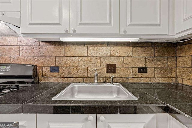 kitchen featuring white cabinetry, tile counters, a sink, and backsplash