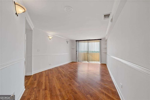 unfurnished room featuring visible vents, crown molding, baseboards, and wood finished floors