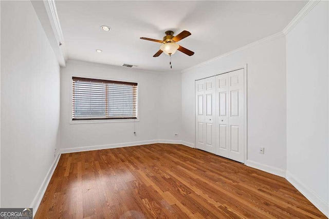 unfurnished bedroom featuring baseboards, ornamental molding, wood finished floors, and a closet