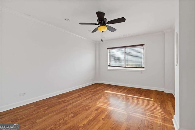spare room with a ceiling fan, wood finished floors, baseboards, visible vents, and ornamental molding