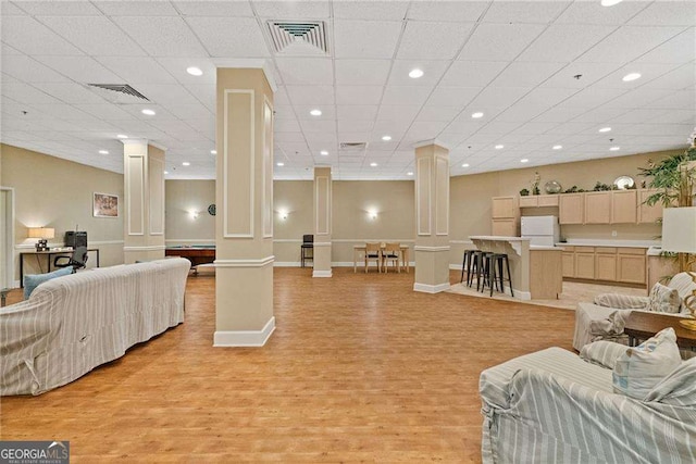 living room featuring light wood finished floors, visible vents, and ornate columns
