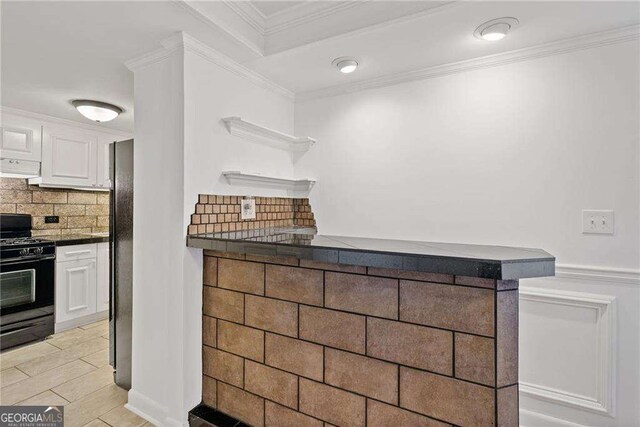 kitchen featuring white cabinetry, crown molding, under cabinet range hood, dark countertops, and black appliances