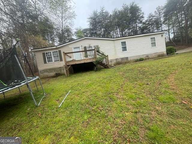 back of house with a deck, a trampoline, a lawn, and crawl space