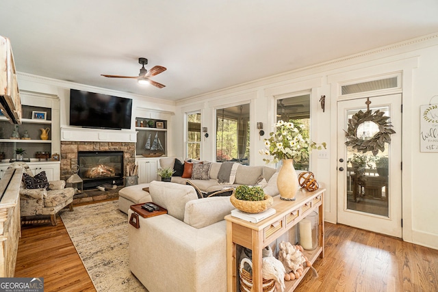 3227 Aviary Ct NW, Acworth, GA 30101 - living room featuring ceiling fan, ornamental molding, light wood-type flooring, a stone fireplace, and built in shelves