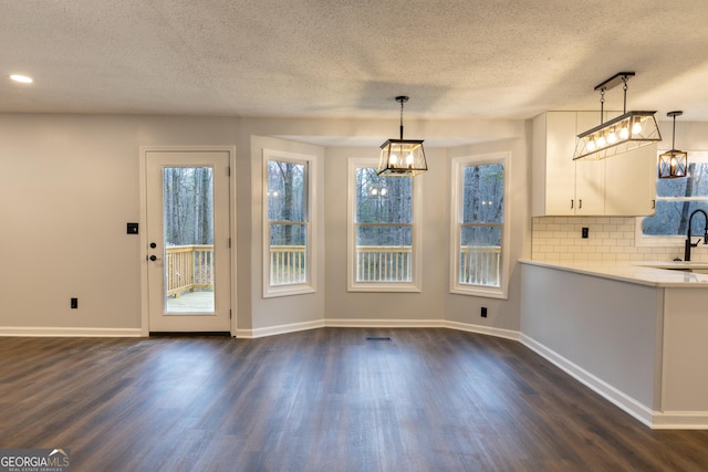 unfurnished dining area with dark wood finished floors, a healthy amount of sunlight, and a textured ceiling
