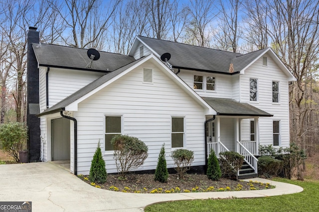 traditional-style house with a porch, a shingled roof, a chimney, and concrete driveway