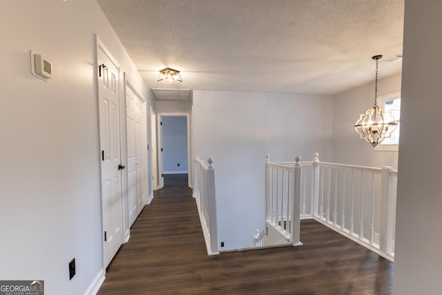 hallway with a chandelier, wood finished floors, a textured ceiling, and an upstairs landing