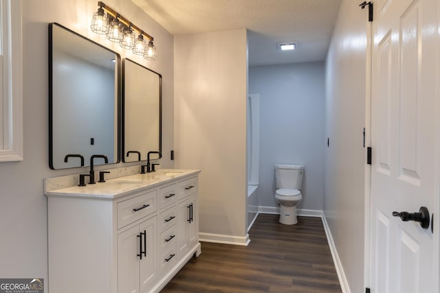 full bath featuring toilet, wood finished floors, a sink, double vanity, and baseboards