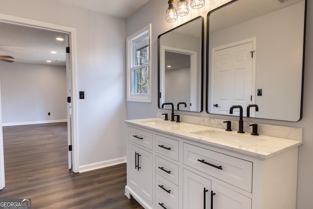 full bathroom with double vanity, baseboards, wood finished floors, and a sink