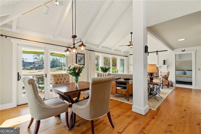 dining area with rail lighting, a barn door, light wood-type flooring, and beam ceiling