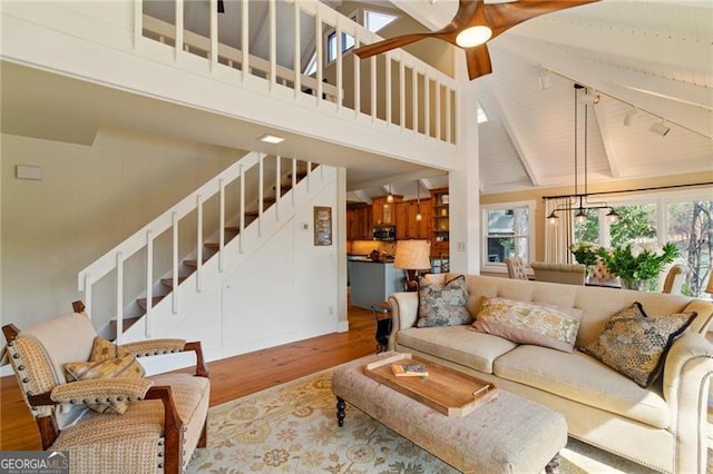 living room featuring ceiling fan, beam ceiling, wood finished floors, stairs, and high vaulted ceiling