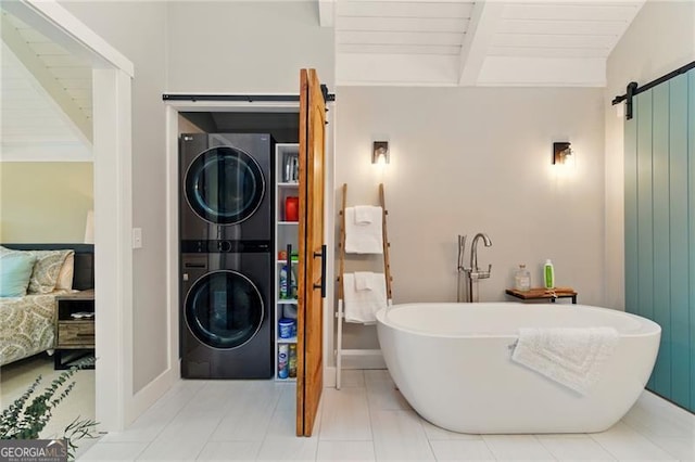 clothes washing area with baseboards, stacked washer and dryer, a barn door, laundry area, and wooden ceiling