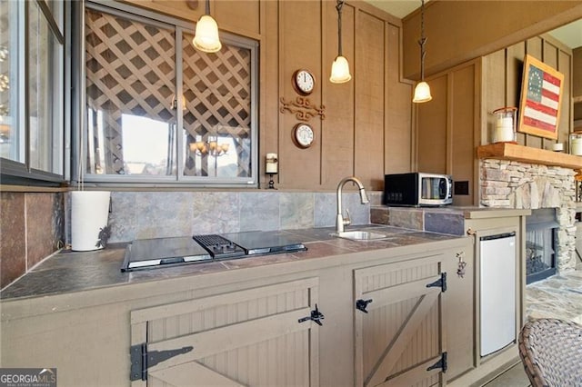 kitchen featuring stainless steel microwave, backsplash, black electric cooktop, pendant lighting, and a sink