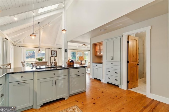 kitchen with vaulted ceiling with beams, light wood-style floors, a sink, and dark countertops