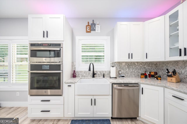 kitchen with white cabinets, light wood finished floors, stainless steel appliances, glass insert cabinets, and a sink
