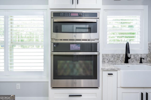 kitchen with white cabinets, a sink, double oven, and light stone counters
