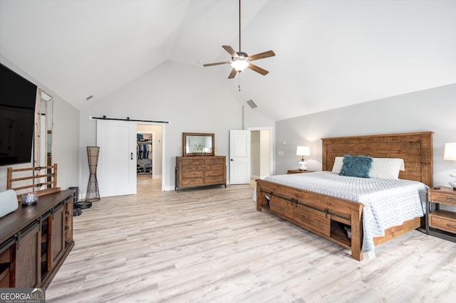 bedroom with high vaulted ceiling, a barn door, a spacious closet, light wood-style floors, and ceiling fan
