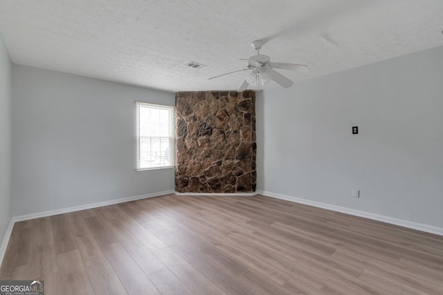 empty room featuring wood finished floors, a textured ceiling, baseboards, visible vents, and ceiling fan