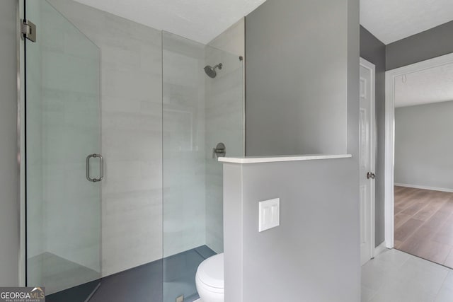 bathroom featuring a textured ceiling, baseboards, a tile shower, toilet, and wood finished floors