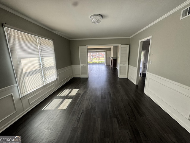 spare room featuring dark wood-style floors, visible vents, a decorative wall, and wainscoting