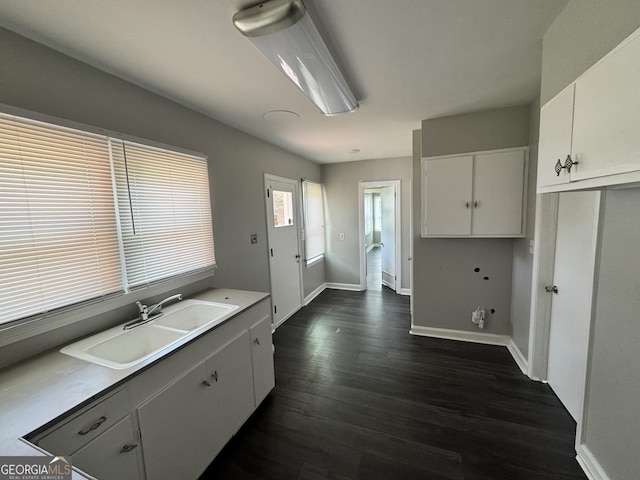 kitchen featuring white cabinetry, light countertops, baseboards, a sink, and dark wood-style floors