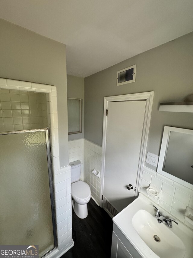 bathroom with a wainscoted wall, toilet, a shower stall, visible vents, and tile walls