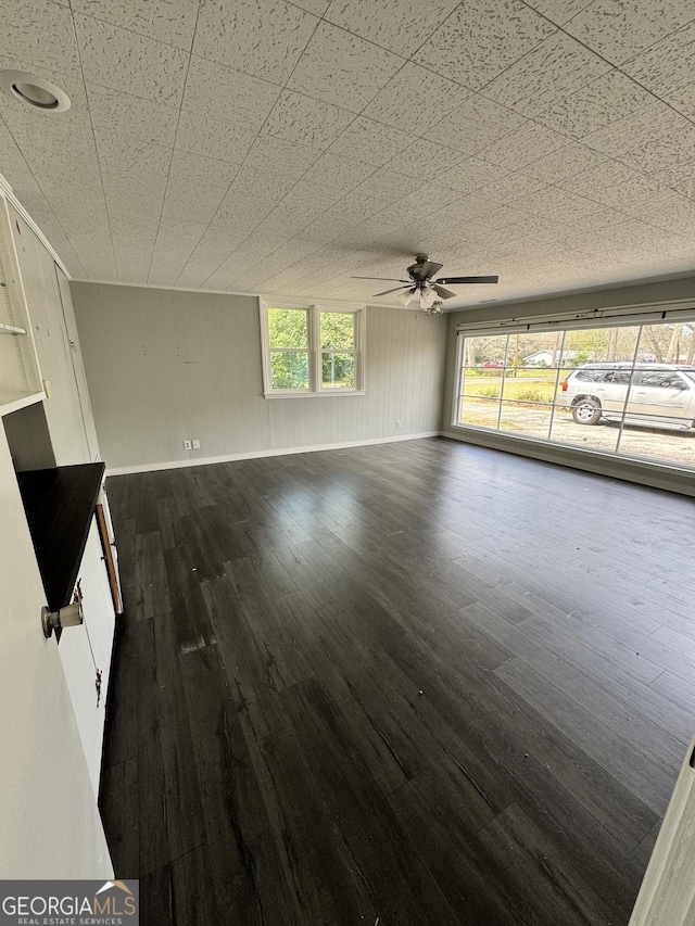 unfurnished living room with plenty of natural light, dark wood-style floors, baseboards, and ceiling fan
