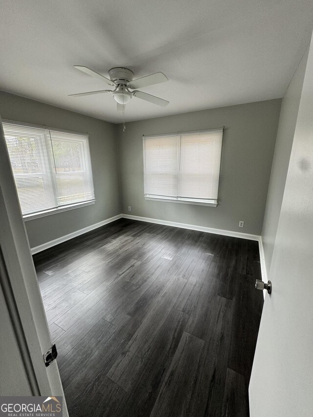 empty room with baseboards, ceiling fan, and dark wood finished floors