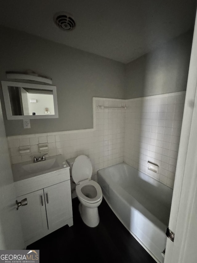 full bathroom with toilet, a tub to relax in, vanity, visible vents, and tile walls