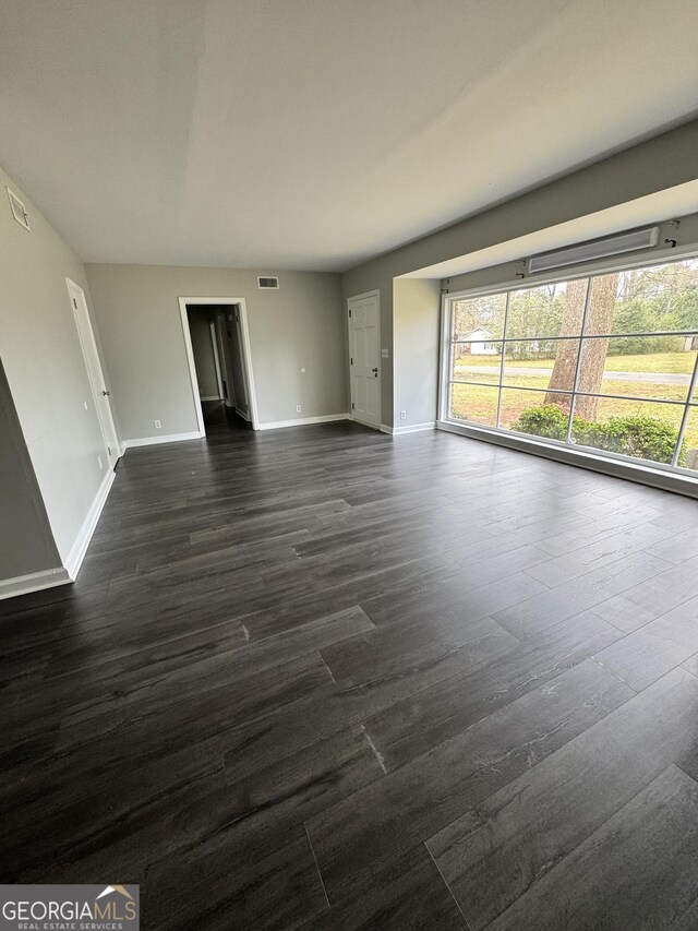unfurnished living room with dark wood finished floors, a wealth of natural light, visible vents, and baseboards