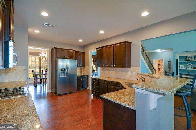 kitchen featuring visible vents, light stone counters, a sink, stainless steel appliances, and dark wood-style floors