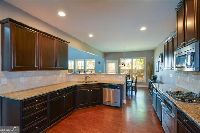 kitchen featuring dark wood-style flooring, light stone counters, a peninsula, appliances with stainless steel finishes, and a sink