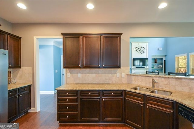 kitchen with a sink, backsplash, dark brown cabinetry, and light stone counters