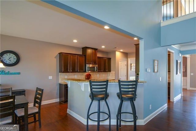 kitchen featuring stainless steel microwave, tasteful backsplash, dark wood-style flooring, and a kitchen bar