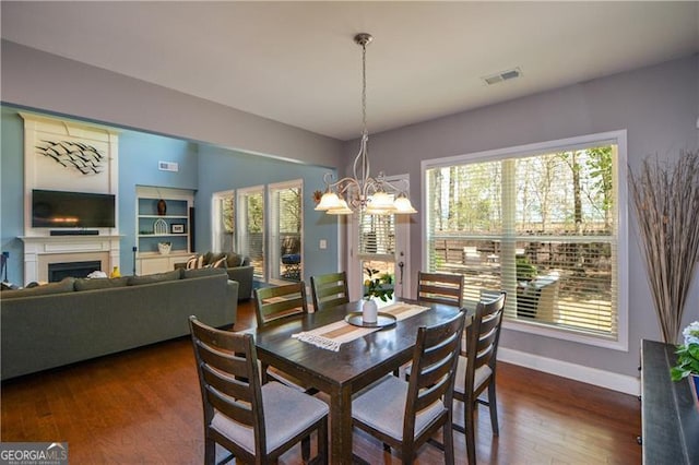 dining room featuring a notable chandelier, baseboards, a fireplace, visible vents, and wood finished floors