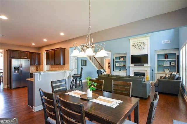 dining area featuring a notable chandelier, recessed lighting, a fireplace, visible vents, and dark wood finished floors