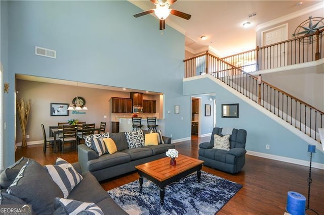 living area with a high ceiling, ceiling fan, visible vents, and wood finished floors